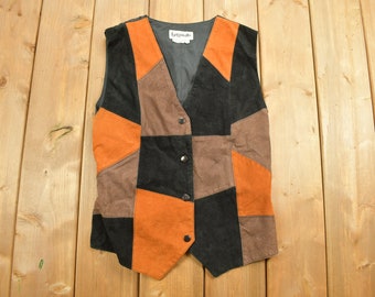 May include: A brown, black and orange suede vest with a V-neck and button closure. The vest is made of different coloured suede patches sewn together.