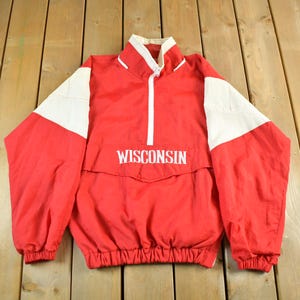 Op de afbeelding: Rode en witte vintage jas met het woord "WISCONSIN" op de borst gedrukt. De jas heeft een witte rits, witte accenten op de schouders en een witte kraag. Gemaakt van een lichtgewicht materiaal.
