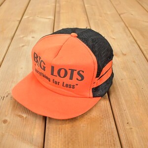 May include: An orange and black trucker hat featuring the text "BIG LOTS" and "everything for Less". The hat has a mesh back and a curved peak.