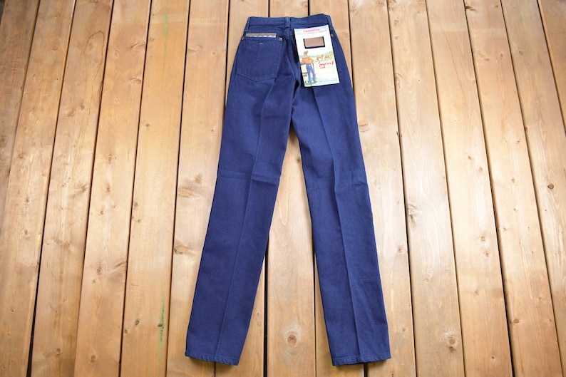 May include: A pair of dark blue denim jeans with a brown leather patch on the back pocket. The jeans have a straight leg and a classic fit.