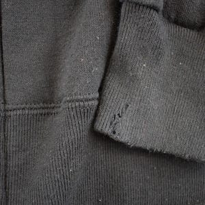 May include: Close-up of a dark gray zip-up hoodie. The image shows the fabric texture, seams, and a torn cuff. The hoodie appears to be well-worn, with visible wear and tear on the sleeve.