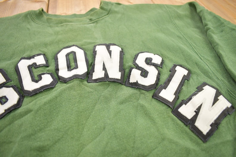 May include: Green sweatshirt with the word "WISCONSIN" in white letters with black outlines.