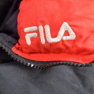 May include: Close-up of a black and red jacket with a white embroidered FILA logo on the red section.