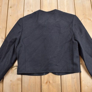 K&ouml;nnte beinhalten: Schwarzer Blazer mit langen &Auml;rmeln, von hinten betrachtet. Die Jacke hat ein klassisches Design mit rundem Ausschnitt und taillierter Passform. Der Stoff ist dunkel und einfarbig, geeignet f&uuml;r formelle oder halbformelle Anl&auml;sse.