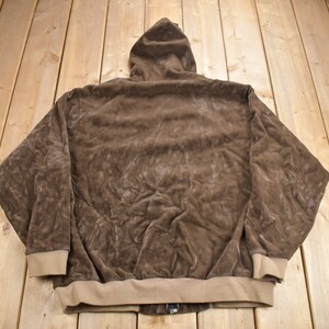 May include: A brown hooded sweatshirt with a zipper closure. The sweatshirt is made of a soft, plush fabric.