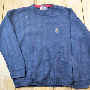 May include: A navy blue sweater with a small embroidered logo on the chest. The logo is green, red, and white. The sweater is made of a soft, comfortable material.