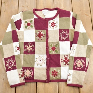 Könnte beinhalten: Ein rot-weiß-grüner Cardigan mit Karomuster und Blumenstickerei. Der Cardigan hat einen Knopfverschluss.