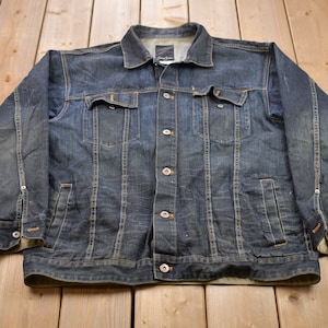 May include: A dark blue denim jacket with a button closure and multiple pockets. The jacket has a faded look and is made of a thick, durable material.