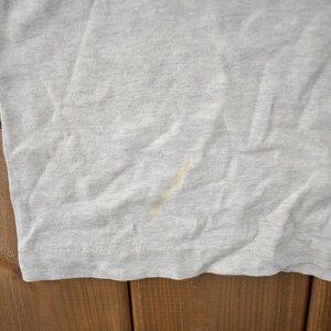 May include: A close-up of a light grey t-shirt with a small yellow stain.