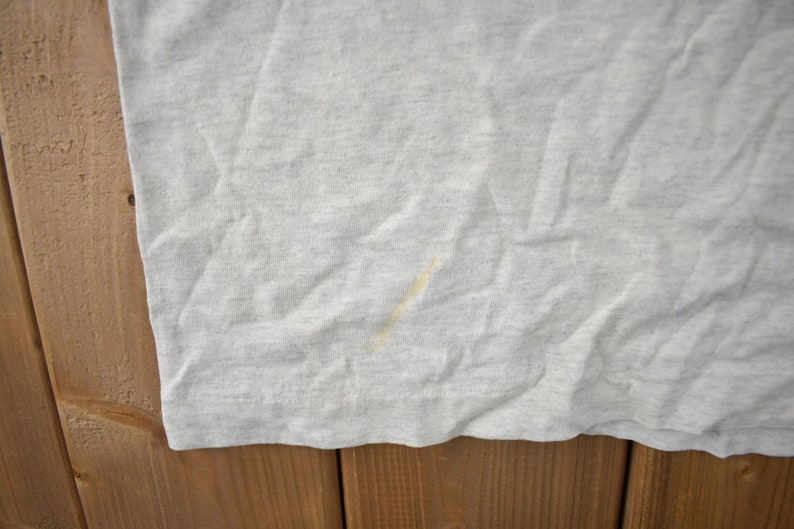 May include: A close-up of a light grey t-shirt with a small yellow stain.