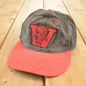 Könnte beinhalten: Vintage Baseballkappe mit grauem Oberteil und rotem Schirm. Die Kappe zeigt einen großen roten Buchstaben "V" mit einem teuflischen Maskottchen-Design. Der Hut ist wahrscheinlich aus Baumwolle oder einem ähnlichen Stoff.