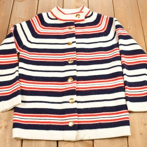May include: A white, blue, and red striped cardigan with gold buttons. The cardigan has a round neckline and long sleeves.