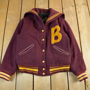 May include: Maroon hooded varsity jacket with a large yellow "B" patch. The jacket features a yellow and maroon striped trim on the cuffs and waist, and a yellow stripe on the hood. The jacket has a button-up front and two front pockets.