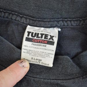 May include: Black T-shirt with a white Tultex tag that reads "100% Cotton/Algodon/Coton Preshrunk" and "Fabric Made in USA Sewn in Canada/En Canada Tissu Fabrique aux E.U./Tela Mecho en EUA Cosida et Cousu au Canada" and "X-Large/Extra Grande/X Grand".
