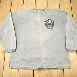 Puede incluir: Sudadera gris de manga larga con mangas acanaladas. La parte delantera presenta un gr&aacute;fico de "Pesadilla antes de Navidad" con Jack Skellington. La camisa tiene cuello redondo y un ajuste relajado.
