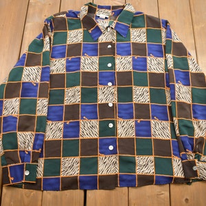 May include: A long-sleeved button-up shirt with a checkered pattern in shades of blue, green, brown, and white. The pattern features a zebra stripe design within each square.