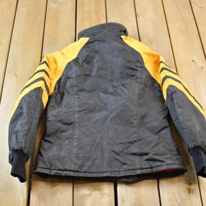 May include: Black jacket with yellow stripes on the sleeves. The jacket has a zipper closure and a high collar.