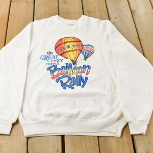 May include: White sweatshirt featuring a colorful hot air balloon graphic with the text "The Great I NY Matville Balloon Rally". The design includes a large orange and yellow balloon and a smaller blue and red balloon.