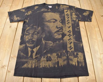 Pode incluir: Camiseta preta com uma estampa desbotada de Martin Luther King Jr. e as palavras "I Have A Dream".