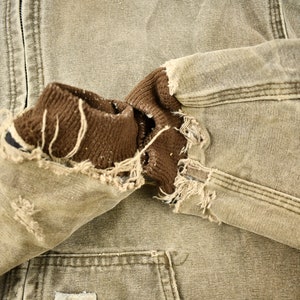 Może przedstawiać: Brązowa i beżowa kurtka robocza z brązowym polarem. Kurtka ma dużą dziurę w rękawie, odsłaniając polarowe podszewki.