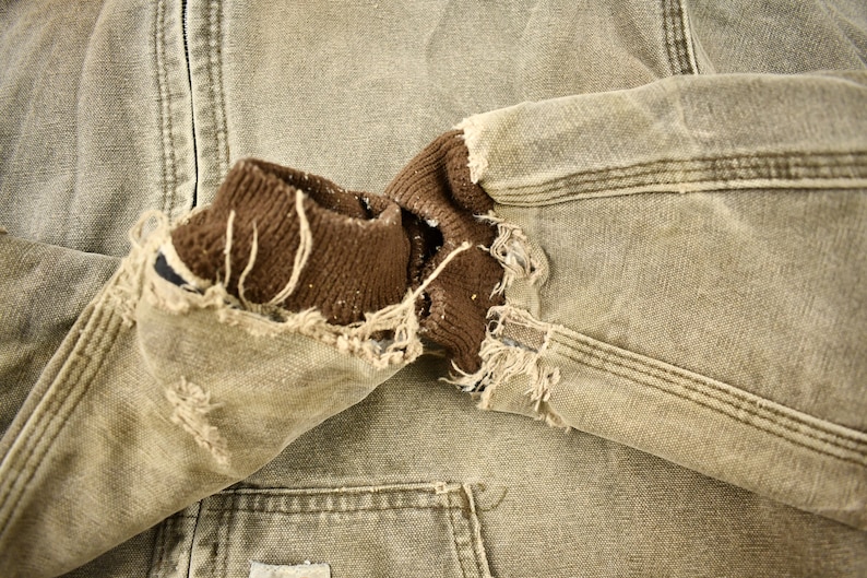 Może przedstawiać: Brązowa i beżowa kurtka robocza z brązowym polarem. Kurtka ma dużą dziurę w rękawie, odsłaniając polarowe podszewki.