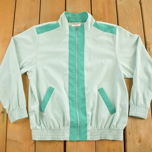 May include: A light blue and teal striped jacket with a zipper closure and two pockets. The jacket has a ribbed waistband and cuffs.