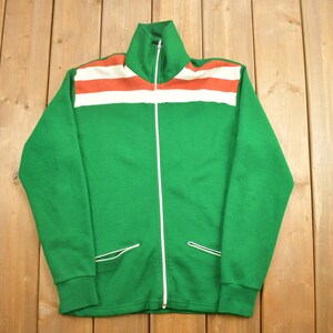 May include: A green zippered jacket with white and orange stripes across the chest. The jacket has two pockets on the front.