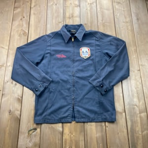 May include: A dark blue work jacket with a zip closure. The jacket has a patch on the left chest with the text "LA Brewers" and a red embroidered name "Mike" on the left side.