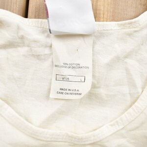 May include: White tank top with a white tag that reads "100% cotton exclusive of decoration A505 L Made in U.S.A. Care on reverse"