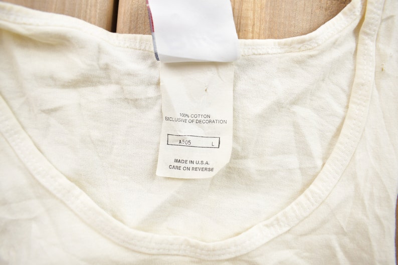 May include: White tank top with a white tag that reads "100% cotton exclusive of decoration A505 L Made in U.S.A. Care on reverse"