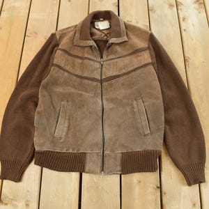 May include: Brown suede jacket with a zip-up front, ribbed knit cuffs, and a collar. The jacket features a suede front with horizontal stitched detailing and two front pockets. The sleeves are a darker brown knit material.