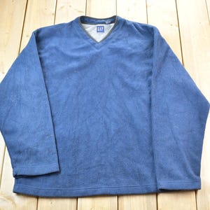 May include: A blue long-sleeved fleece sweater with a v-neck and the word "GAP" on the tag.