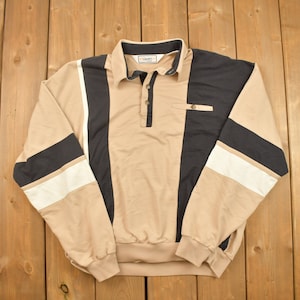 May include: A long-sleeved collared shirt with a striped pattern in beige, black, and white. The shirt has a button-up closure and a small pocket on the chest.