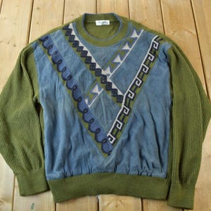 May include: A green and blue sweater with a geometric pattern. The sweater has a crew neck and long sleeves.