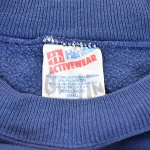 May include: A blue Hanes Activewear sweatshirt tag with white text. The tag says "Hanes Activewear", "60% Cotton (Cotton/Godon)", "50% Polyester", "Made in USA Fabrique aux E-U", "Hecho en los EUA", "Petit/Chico", and "Small".