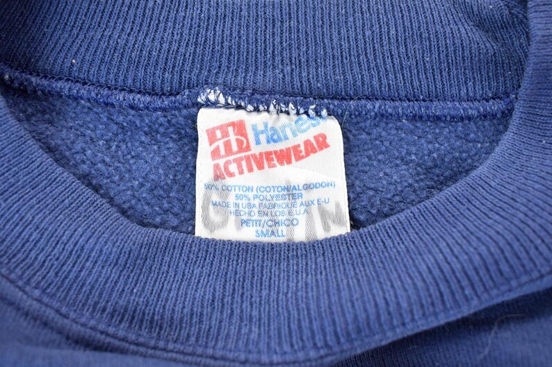 May include: A blue Hanes Activewear sweatshirt tag with white text. The tag says "Hanes Activewear", "60% Cotton (Cotton/Godon)", "50% Polyester", "Made in USA Fabrique aux E-U", "Hecho en los EUA", "Petit/Chico", and "Small".