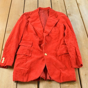 May include: A bright red blazer featuring a notched lapel, a single front button closure, and two flap pockets. The sleeves are finished with three small gold-toned buttons at each cuff. The garment has a structured collar and long sleeves.