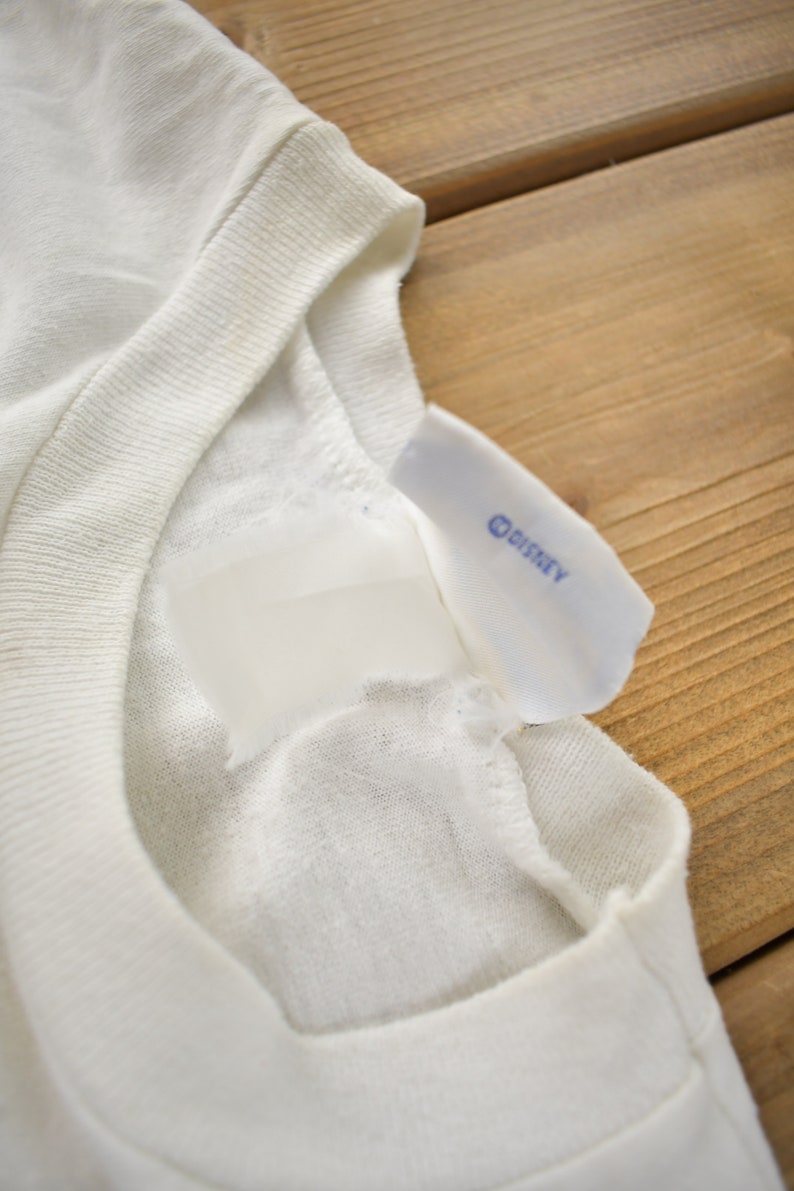 May include: White t-shirt with a white tag and a blue "DISNEY" label.