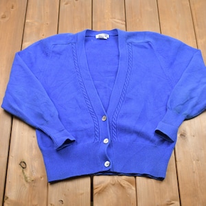 May include: A blue knitted cardigan with a cable knit design and button closure.