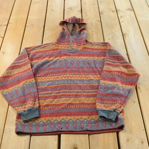 May include: A vintage pullover hoodie with a colorful geometric pattern. The hoodie features a half-zip closure, a hood, and ribbed cuffs. The color palette includes red, blue, orange, and yellow. The garment is made of a soft, textured material.