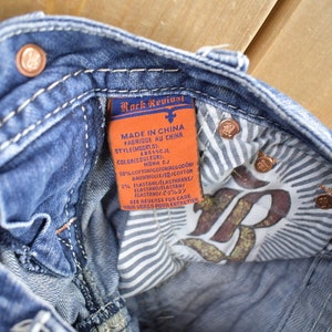 K&ouml;nnte beinhalten: Eine Nahaufnahme des Innenfutters einer blauen Jeans. Die Jeans hat ein wei&szlig;-blaues gestreiftes Futter und ein braunes Leder-Etikett mit dem Text "Rock Revival" und Pflegehinweisen in Englisch, Franz&ouml;sisch und Japanisch.