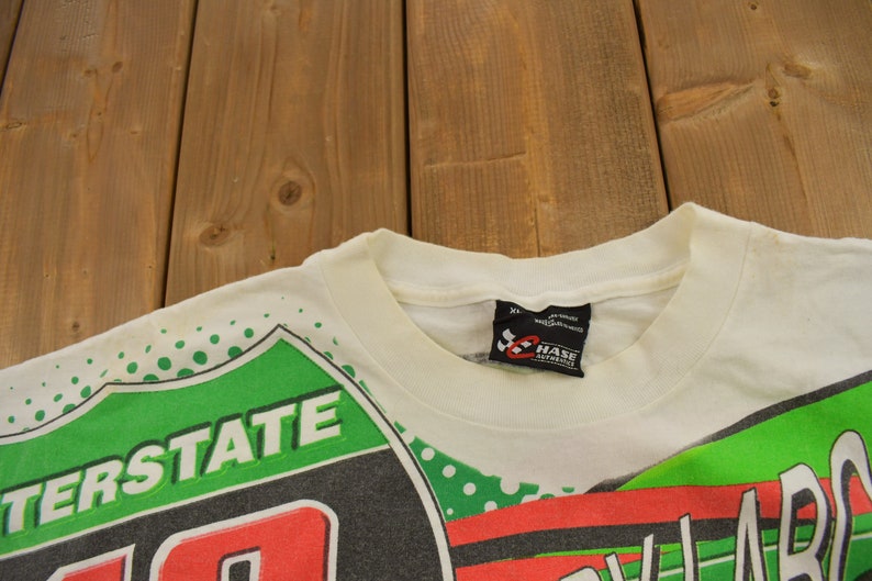 May include: White t-shirt with a green, red and black graphic print featuring the words "Interstate" and "Chase Automotive".