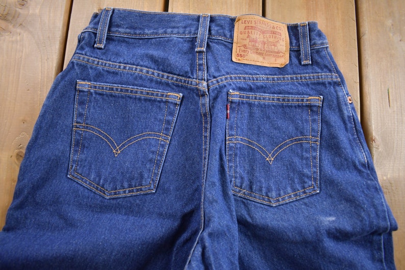 May include: A pair of blue denim jeans with a brown leather Levi's patch on the back pocket. The patch has the text "Levi Strauss & Co. Quality Clothing" and "Every Garment Guaranteed 550".