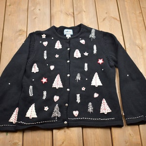 May include: Black cardigan sweater with white and red embroidered Christmas trees, stars, and hearts.