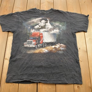 May include: A black t-shirt with a graphic of a white bull jumping over a red semi-truck. The text "Run with the Spirit" is printed on the shirt.