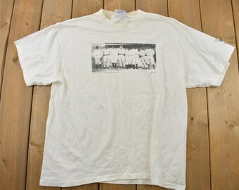Könnte beinhalten: Weißes T-Shirt mit einem Schwarzweißfoto eines Baseballteams auf der Vorderseite. Das Foto zeigt eine Gruppe von Männern in Baseballuniformen, die zusammen stehen. Der Text "The New York Giants 1911 Champions" ist unter dem Foto gedruckt.