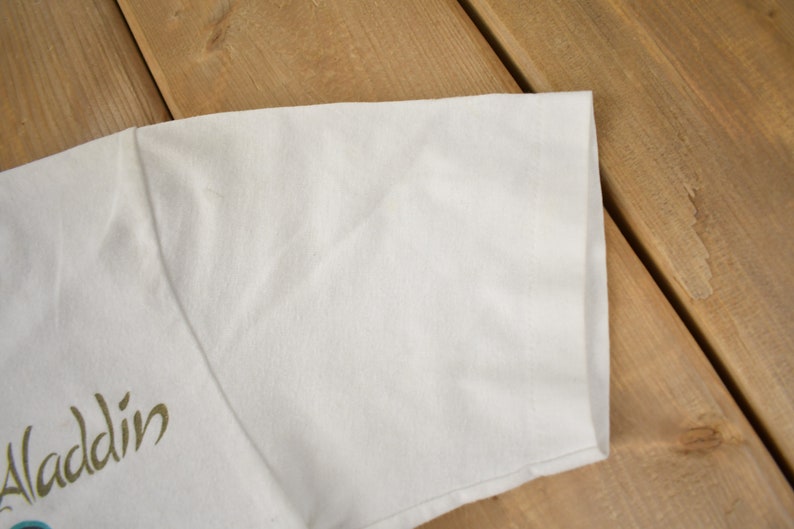 May include: White t-shirt with a gold "Aladdin" graphic on the front.