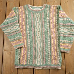 May include: A multi-coloured striped jumper with a crew neck. The jumper is made of a soft, knitted fabric and features a variety of colours, including pink, green, yellow, and white.