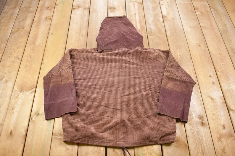 May include: A brown corduroy hoodie with a drawstring. The hoodie has a brown hood and long sleeves.
