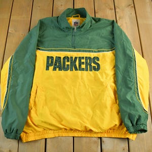 May include: Green and yellow Packers jacket with the team name in large black letters across the chest. The jacket has a half-zip closure and a small NFL logo on the collar.